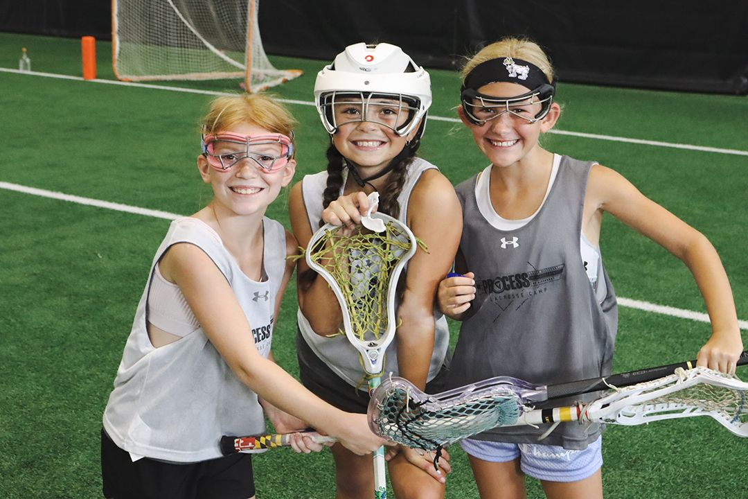 Three girls are posing with a lacrosse stick.