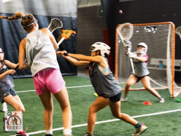 Three women playing lacrosse indoors.